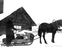 100  Postinkantaja Timo Huusko (8.5.1888 - 22.6.1981) seisoo kotinsa Killilän lumisella pihalla pidellen ohjaksista reen eteen valjastettua Polle-hevosta. Reessä postisäkki. Hevosen takana savusauna, reen takana navetan karjakeittiöpääty.